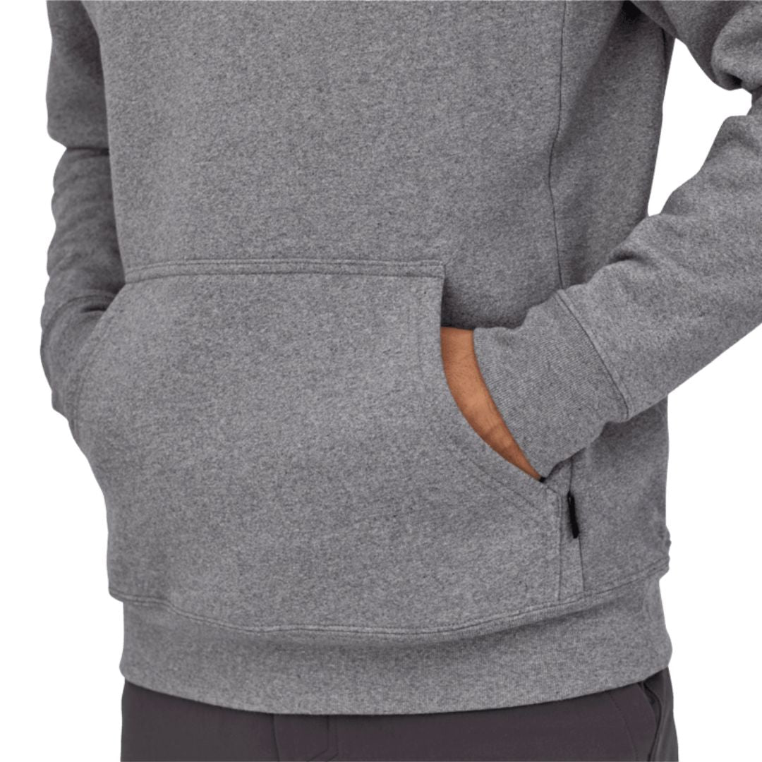 Detalle del bolsillo canguro de la sudadera Patagonia P-6 Label Uprisal Hoody en gris Gravel Heather, mostrado sobre modelo con la mano dentro y bolsillo lateral con cremallera.