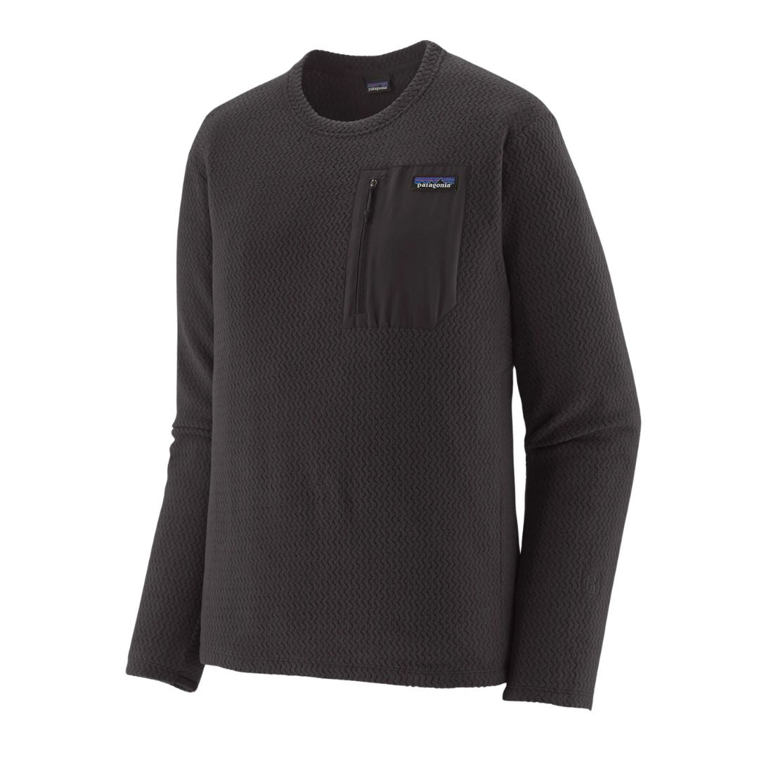 Patagonia M's R1 Air Crew en color negro Black — vista frontal en tres cuartos sin modelo, destacando el tejido jacquard en zigzag de poliéster 100% reciclado, el bolsillo con cremallera en tejido liso negro, la etiqueta Patagonia y el logo R bordado en el bajo lateral.