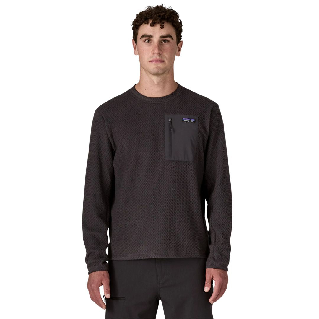 Patagonia M's R1 Air Crew en color negro Black — vista frontal sobre modelo, con tejido jacquard en zigzag de poliéster reciclado y bolsillo con cremallera en el pecho izquierdo en tejido liso negro con etiqueta Patagonia.