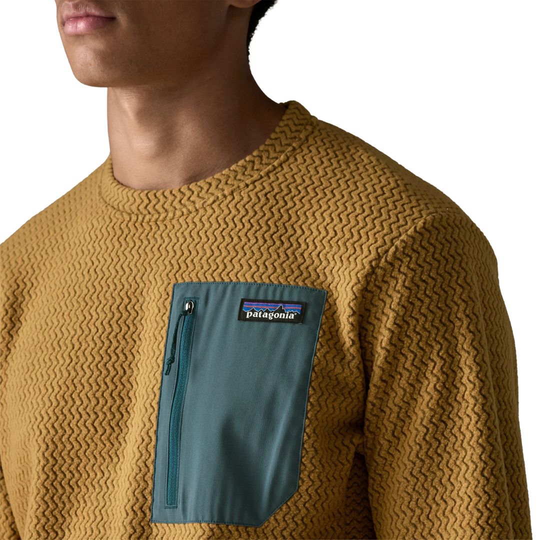 Detalle del bolsillo con cremallera del Patagonia M's R1 Air Crew Bobcat Brown — primer plano del bolsillo en tejido verde azulado con etiqueta Patagonia y textura jacquard en zigzag del forro polar técnico reciclado.