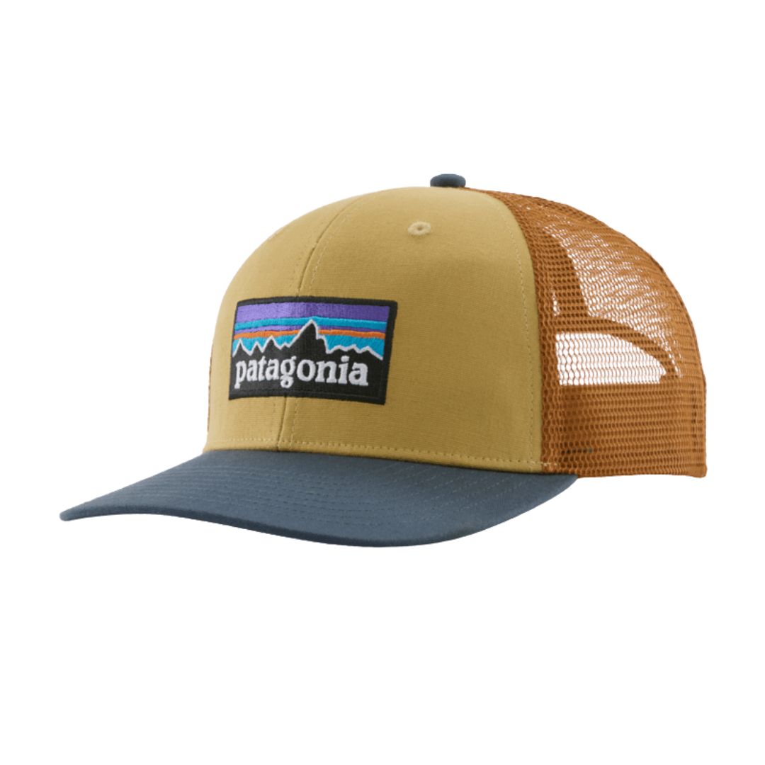 Gorra trucker Patagonia P-6 Logo en color mostaza con visera azul (Lynx Tan), vista de perfil con el parche P-6 bordado y la rejilla de malla naranja.