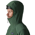 Patagonia R1 TechFace Hoody verde canopy, chaqueta técnica con capucha para hombre. Primer plano de la capucha ajustable puesta sobre un casco, con cordón de ajuste bajo la barbilla.