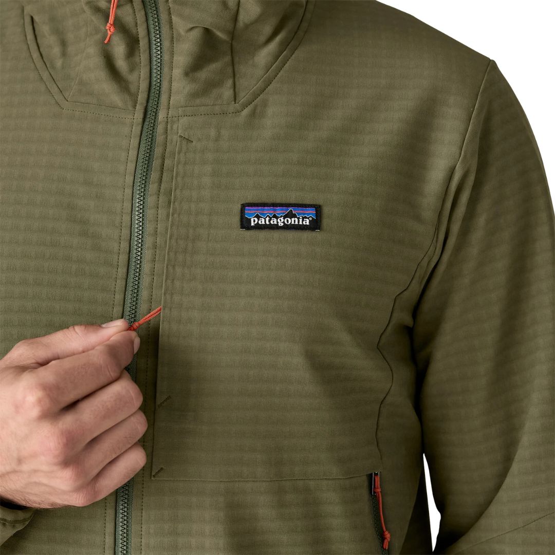 Detalle frontal Patagonia R1® TechFace Hoody: tejido doble en rejilla, bolsillo de pecho exterior con cremallera, parche logo P-6 y tirador de cremallera naranja.