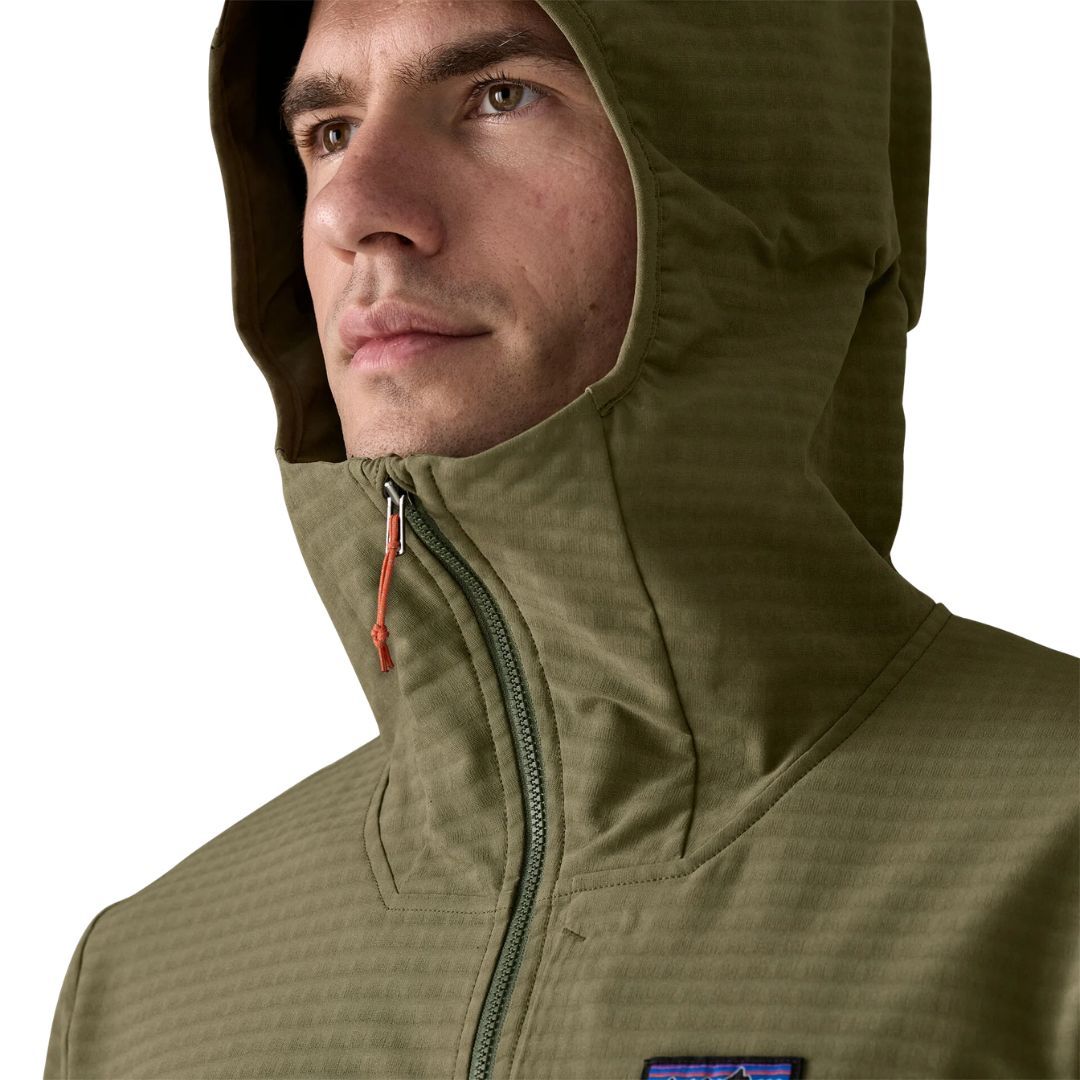 Detalle de capucha Patagonia R1® TechFace Hoody con visera laminada ajustable puesta: interior suave en rejilla visible en cuello y cremallera completa con tirador naranja.