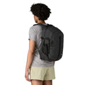 Patagonia Refugio Daypack 26L en color negro, vista trasera con modelo, mostrando correas acolchadas de poliéster reciclado, correa esternal ajustable, bolsillo lateral de malla elástica y etiqueta Patagonia visible.