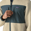 Detalle del pecho de la Patagonia Retro Pile Fleece Patch Jacket en color beige Pelican: panel de ripstop azul pizarra, dos bolsillos con cremallera vertical, parche Patagonia y borreguillo.