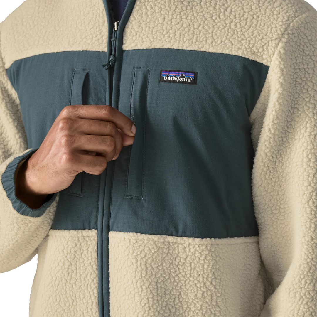 Detalle del pecho de la Patagonia Retro Pile Fleece Patch Jacket en color beige Pelican: panel de ripstop azul pizarra, dos bolsillos con cremallera vertical, parche Patagonia y borreguillo.