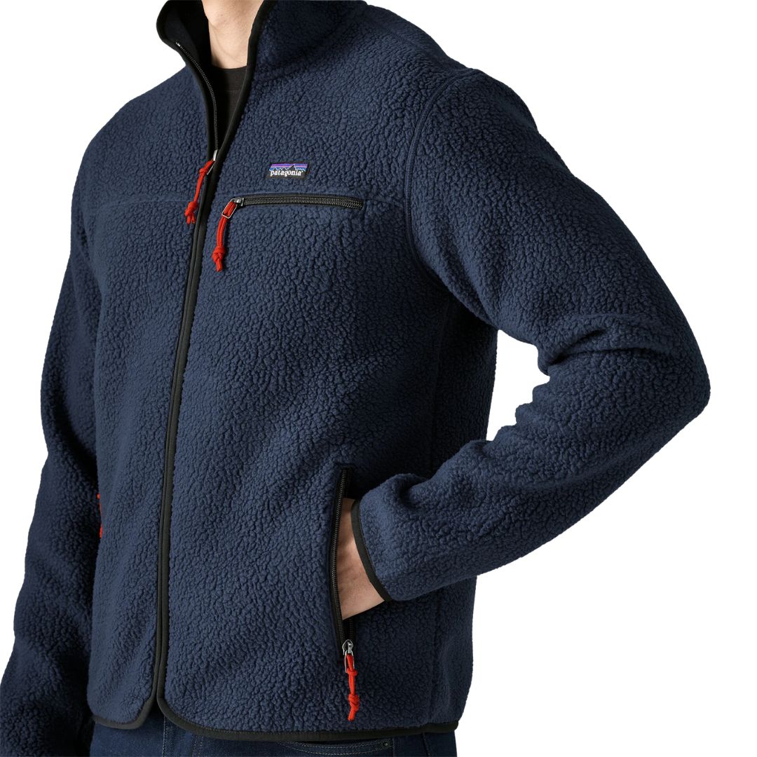 Detalle de la Patagonia Retro Pile Fleece Jacket en color azul marino New Navy: parche Patagonia, bolsillo de pecho con cremallera negra, tiradores rojos y mano en el bolsillo calientamanos.