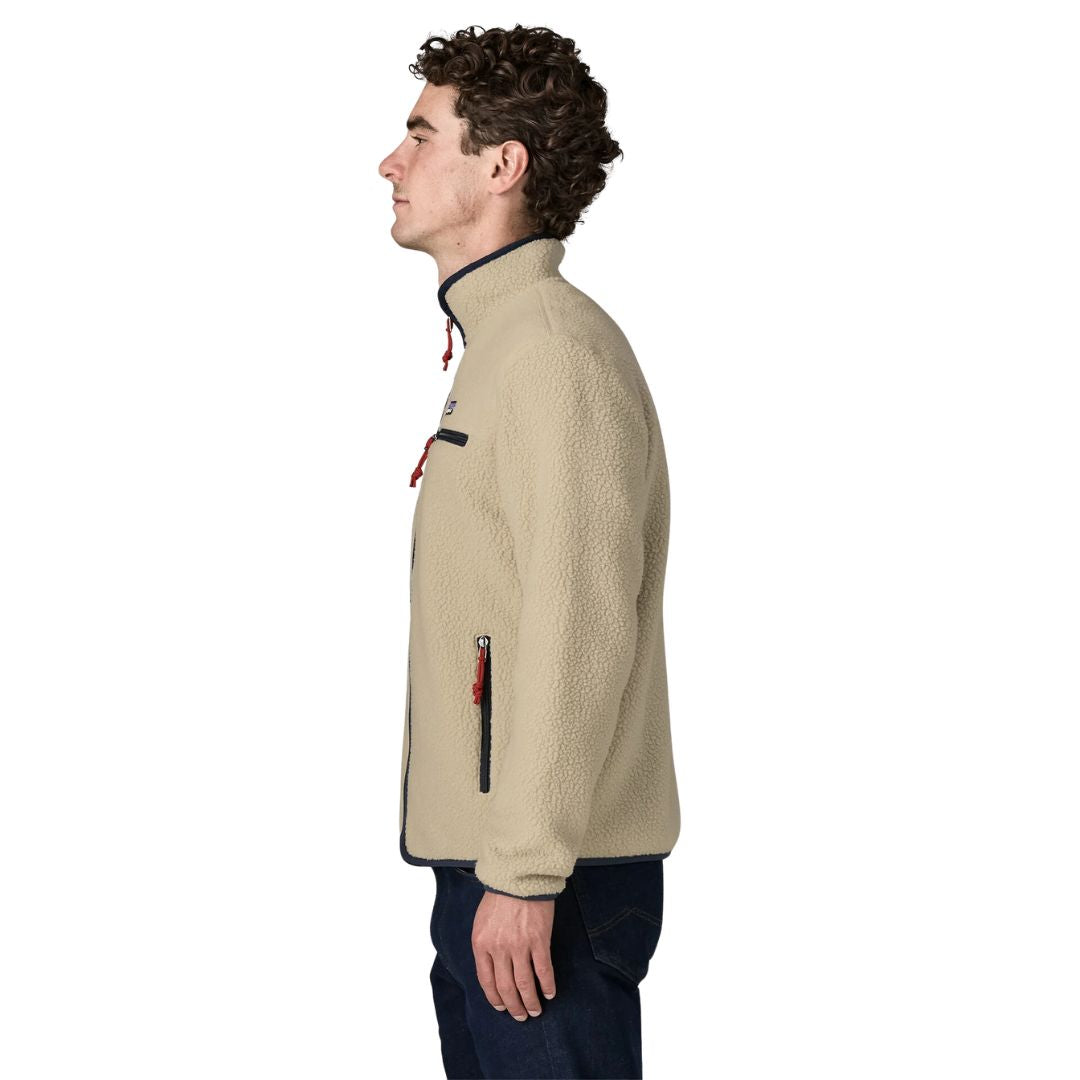 Perfil de la chaqueta polar Patagonia Retro Pile Fleece Jacket en color beige Pelican: cuello alto con ribete azul marino, tiradores rojos y bolsillo calientamanos con cremallera, sobre vaqueros.