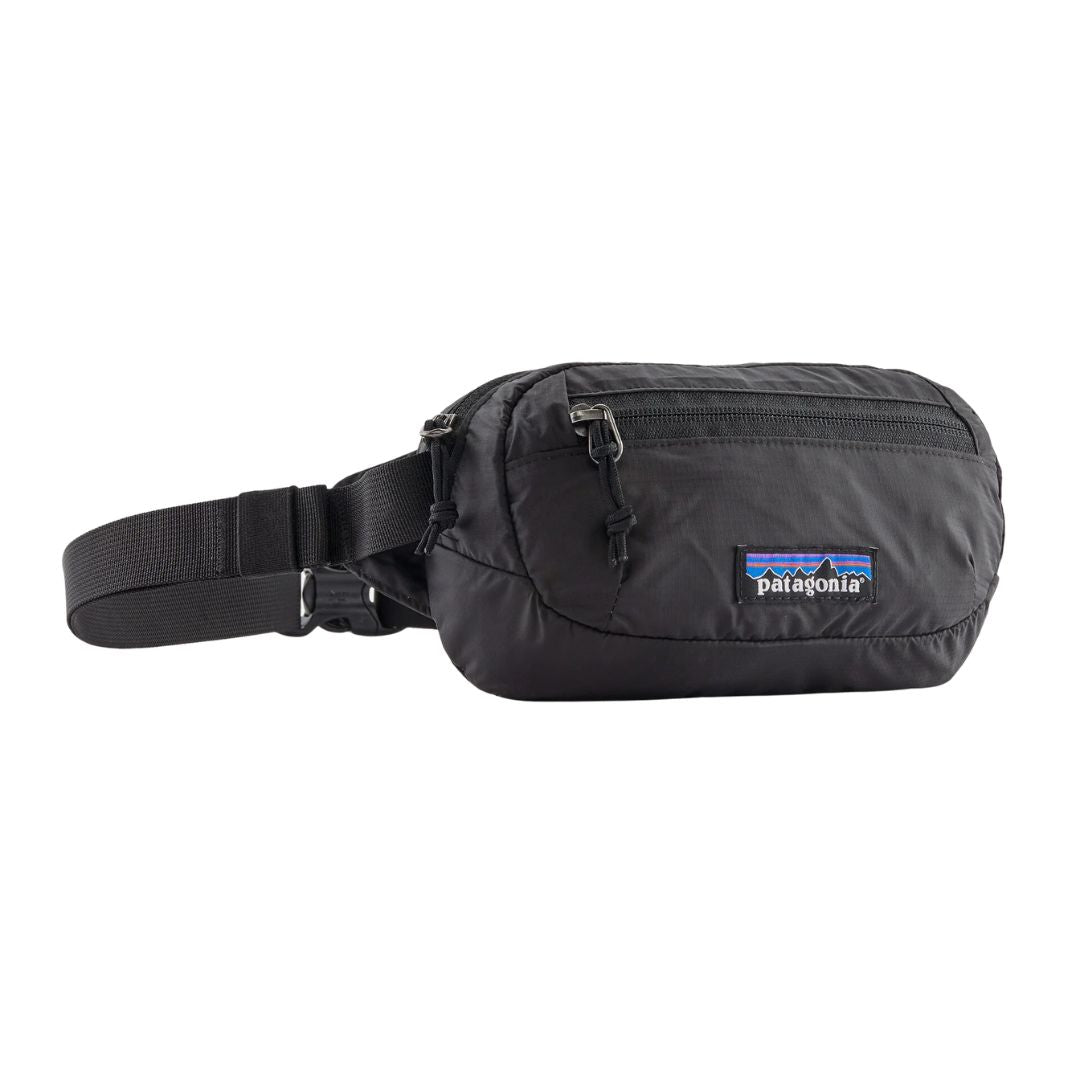 Patagonia Terravia Mini Hip Pack 1L en color negro, vista de producto en tres cuartos sin modelo, mostrando el compartimento principal con cremallera metálica, el bolsillo frontal de seguridad, la etiqueta Patagonia con logo Fitz Roy y la correa de nailon reciclado con ajustador.