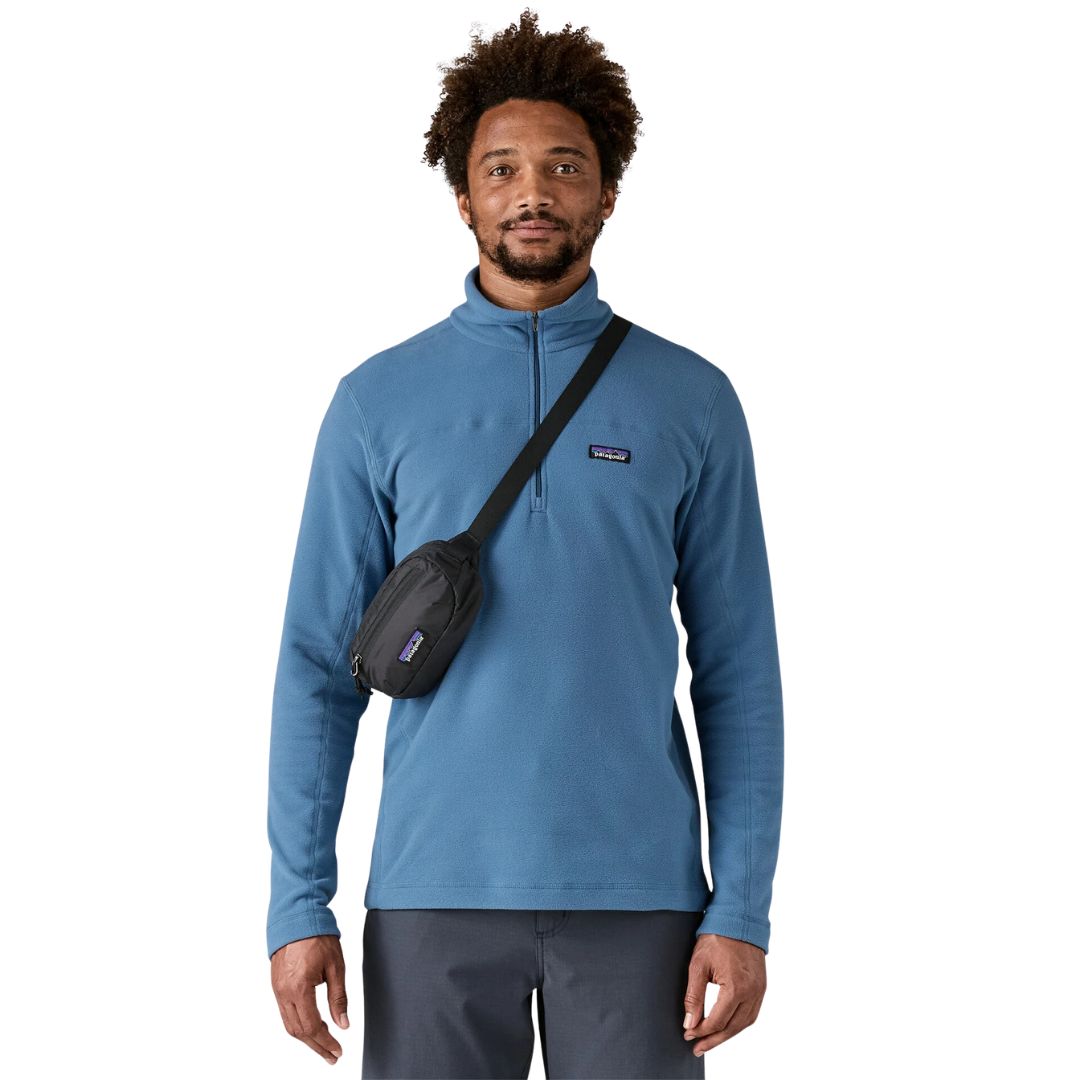 Patagonia Terravia Mini Hip Pack 1L en color negro, vista frontal con modelo llevándola como bolso cruzado en el pecho, mostrando el modo de uso alternativo con la correa ajustada en diagonal, el compartimento principal y la etiqueta Patagonia visible.