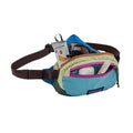 Riñonera Patagonia Terravia Mini Hip Pack en colorway Patchwork Snowmelt Blue, vista de detalle con el bolsillo abierto mostrando gafas de sol, snacks y accesorios en su interior.