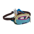 Riñonera Patagonia Terravia Mini Hip Pack en Patchwork: Snowmelt Blue abierta y cargada con gafas de sol, snacks, funda de auriculares y protector labial, mostrando su capacidad.