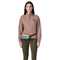 Riñonera Patagonia Terravia Mini Hip Pack en colorway Patchwork Snowmelt Blue, modelo llevándola a la cintura como riñonera clásica sobre un legging verde.