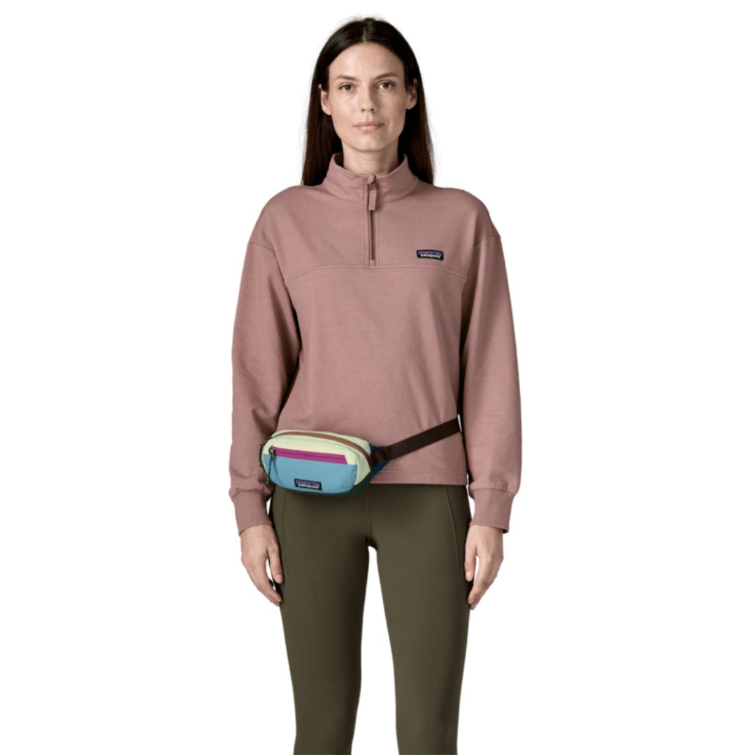 Riñonera Patagonia Terravia Mini Hip Pack en colorway Patchwork Snowmelt Blue, modelo llevándola a la cintura como riñonera clásica sobre un legging verde.