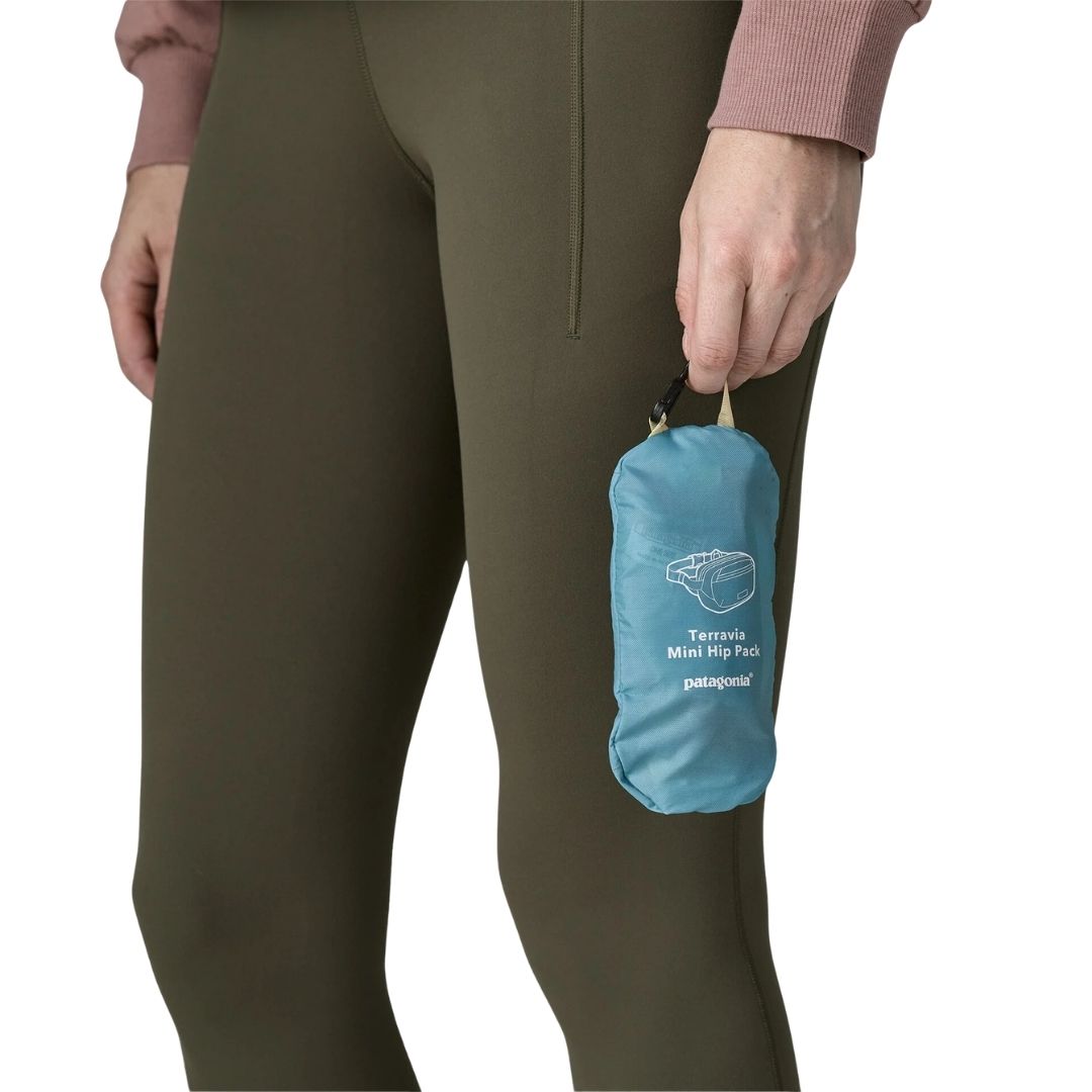 Riñonera Patagonia Terravia Mini Hip Pack en Patchwork: Snowmelt Blue, plegada dentro de su propio bolsillo interior y enganchada a un mosquetón sobre unos leggings.