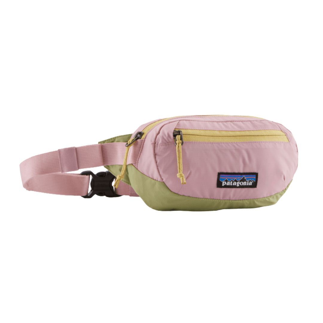 Patagonia Terravia Mini Hip Pack 1L en color quiet violet, vista frontal de producto en tres cuartos sin modelo, mostrando el diseño bicolor en rosa palo y verde oliva con franja amarilla, compartimento principal con cremallera y tirador amarillo, bolsillo frontal de seguridad y etiqueta Patagonia con logo Fitz Roy.