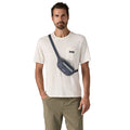 Patagonia Terravia Mini Hip Pack 1L en color smolder blue, vista frontal completa con modelo llevándola como bolso cruzado en el pecho, mostrando el modo de uso alternativo con la correa en diagonal, el tejido ripstop de nailon reciclado azul marino y la etiqueta Patagonia.