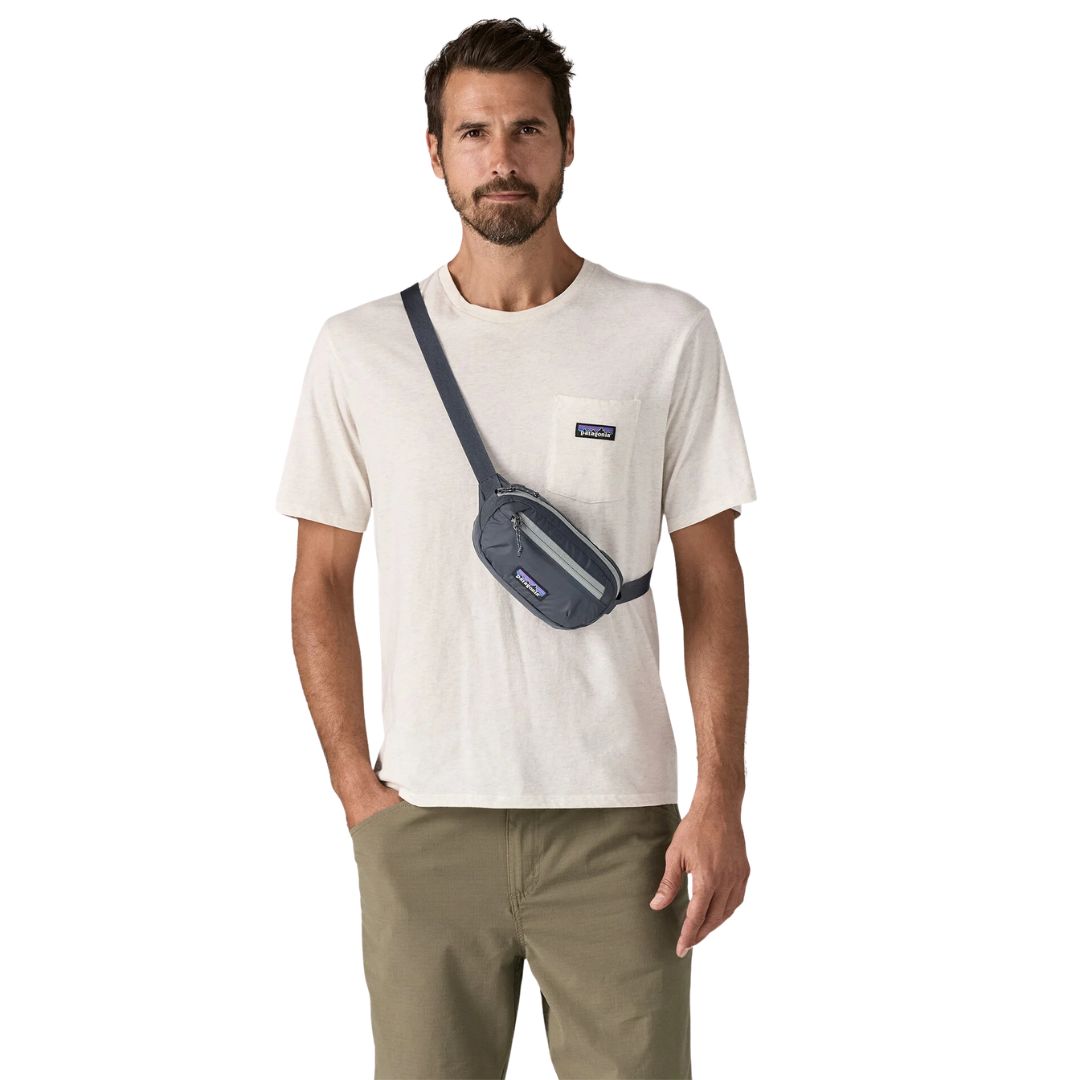 Patagonia Terravia Mini Hip Pack 1L en color smolder blue, vista frontal completa con modelo llevándola como bolso cruzado en el pecho, mostrando el modo de uso alternativo con la correa en diagonal, el tejido ripstop de nailon reciclado azul marino y la etiqueta Patagonia.