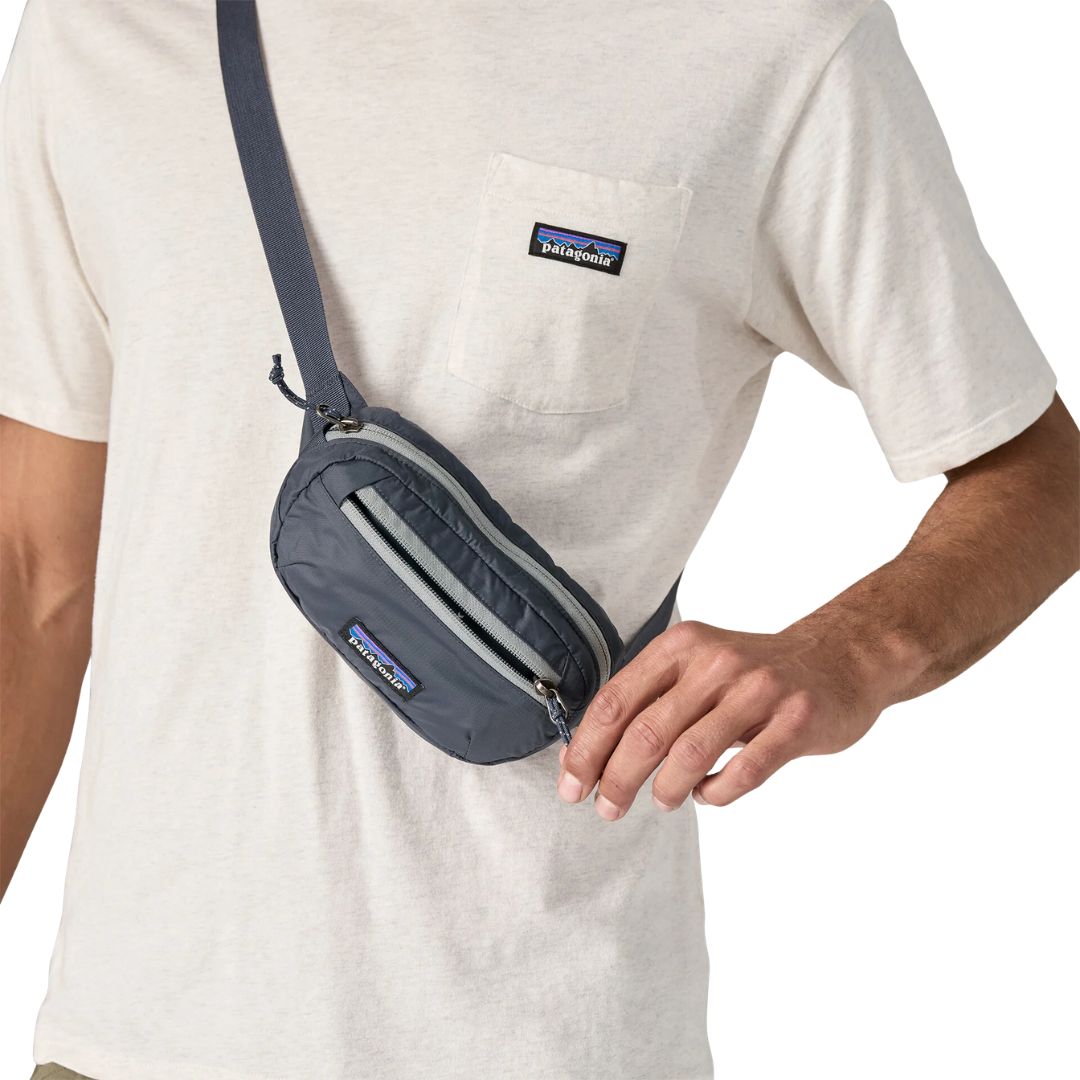 Patagonia Terravia Mini Hip Pack 1L en color smolder blue, detalle del compartimento principal con cremallera y franja gris, llevada como bolso cruzado, mostrando el tamaño compacto de 1 litro sobre el pecho y la etiqueta Patagonia con logo Fitz Roy.