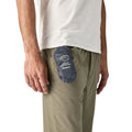 Patagonia Terravia Mini Hip Pack 1L en color smolder blue plegada en su propio bolsillo interior, con el texto Terravia Mini Hip Pack y el logo Patagonia visibles, guardada en el bolsillo lateral del pantalón del modelo para demostrar su diseño ultracompacto y plegable.