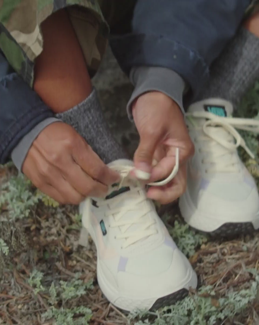 Una chica se ata las Zapatillas de trekking impermeables Vans MTE Crosspath Natural en una playa