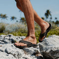 Chanclas Reef Fanning black gum en uso sobre rocas al aire libre.