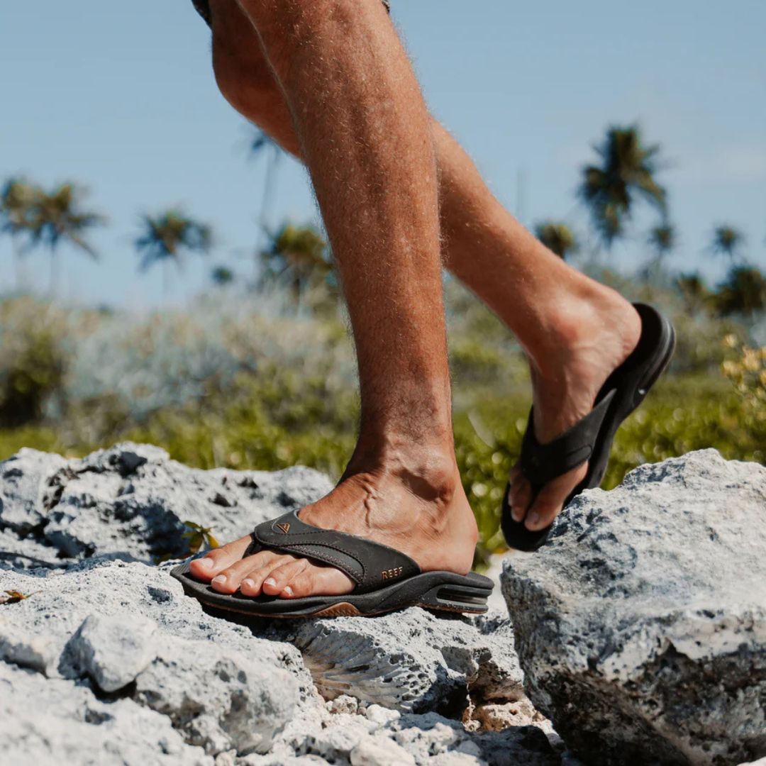 Chanclas Reef Fanning black gum en uso sobre rocas al aire libre.