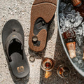 Chanclas Reef Fanning black gum con abridor de botellas integrado en la suela, vista superior y detalle de bebidas.