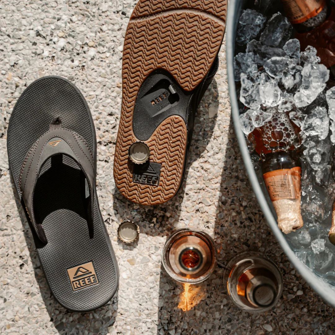 Chanclas Reef Fanning black gum con abridor de botellas integrado en la suela, vista superior y detalle de bebidas.