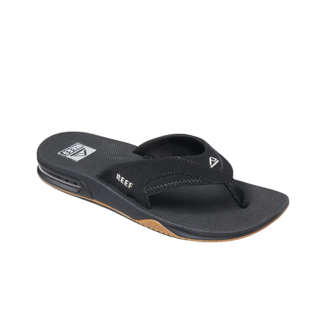 Vista en ángulo de las chanclas REEF Fanning negras con logo visible, plantilla ergonómica y diseño resistente.
