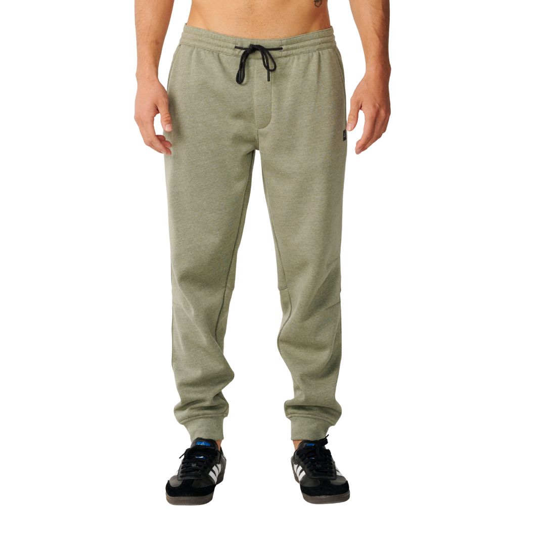 Rip Curl Anti-Series Departed Trackpant en verde surplus, vista frontal sobre modelo, jogger de felpa con cinturilla elástica y cordón negro, bajos con puño.