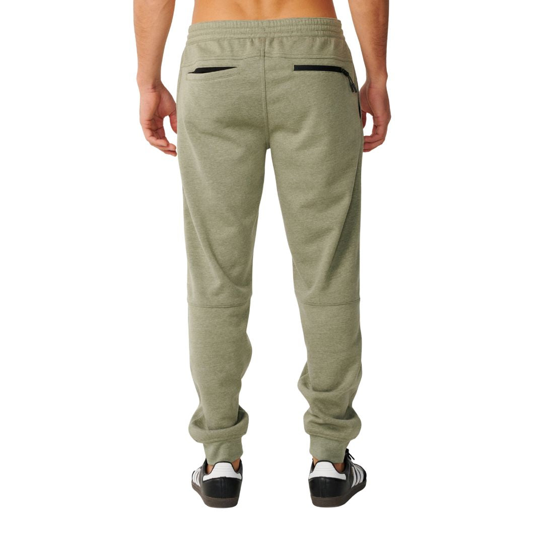 Pantalón Rip Curl Anti-Series Departed en verde surplus, vista trasera completa sobre modelo, con dos bolsillos con cremallera negra y costuras anguladas en los muslos.