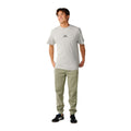 Rip Curl Anti-Series Departed Trackpant en verde surplus, vista completa sobre modelo con camiseta gris, mostrando silueta jogger con puños en el bajo y etiqueta lateral.