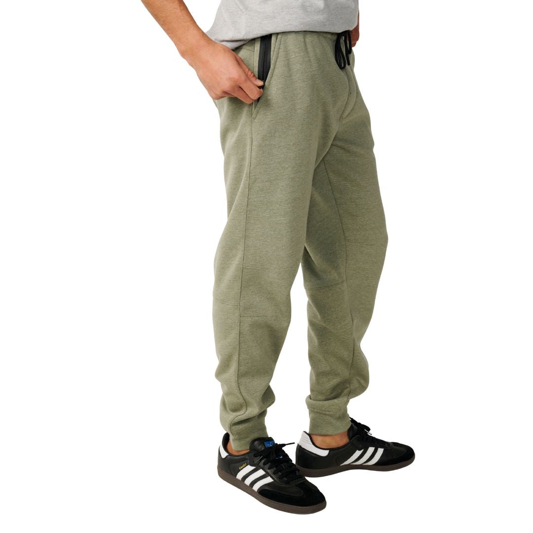 Pantalón de chándal Rip Curl Anti-Series Departed en verde surplus, vista lateral sobre modelo, mostrando bolsillo con cremallera negra en la cintura y puño en el bajo.