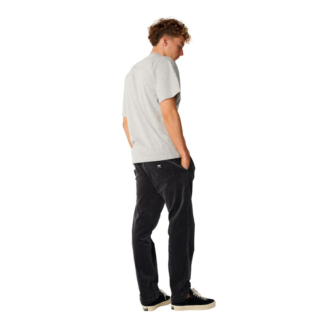 Rip Curl Classic Surf Cord Beach Pant en Washed Black combinado con camiseta gris, vista trasera de cuerpo entero.