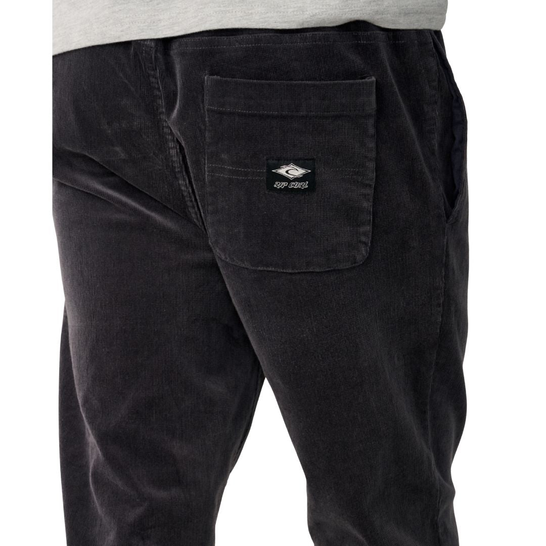 Detalle del bolsillo trasero con solapa del Rip Curl Classic Surf Cord Beach Pant en Washed Black, con la etiqueta tejida Rip Curl y el acabado en pana.