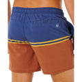 Detalle trasero bañador surf Rip Curl Combine Volley baked clay, bolsillo velcro azul marino, logo sol bordado azul claro y rayas doradas sobre panel terracota.