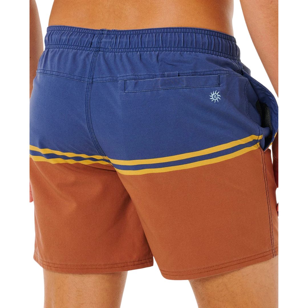 Detalle trasero bañador surf Rip Curl Combine Volley baked clay, bolsillo velcro azul marino, logo sol bordado azul claro y rayas doradas sobre panel terracota.