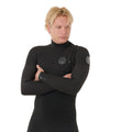 Neopreno surf hombre negro Rip Curl E-Bomb Zip Free 3/2, retrato frontal con brazos cruzados, logo circular en pecho, etiqueta E-Bomb en puño y sistema zip free.