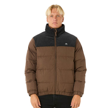 Modelo luciendo la chaqueta Rip Curl Fade Out Cord Puffer marrón y negra, con cremallera hasta el cuello.