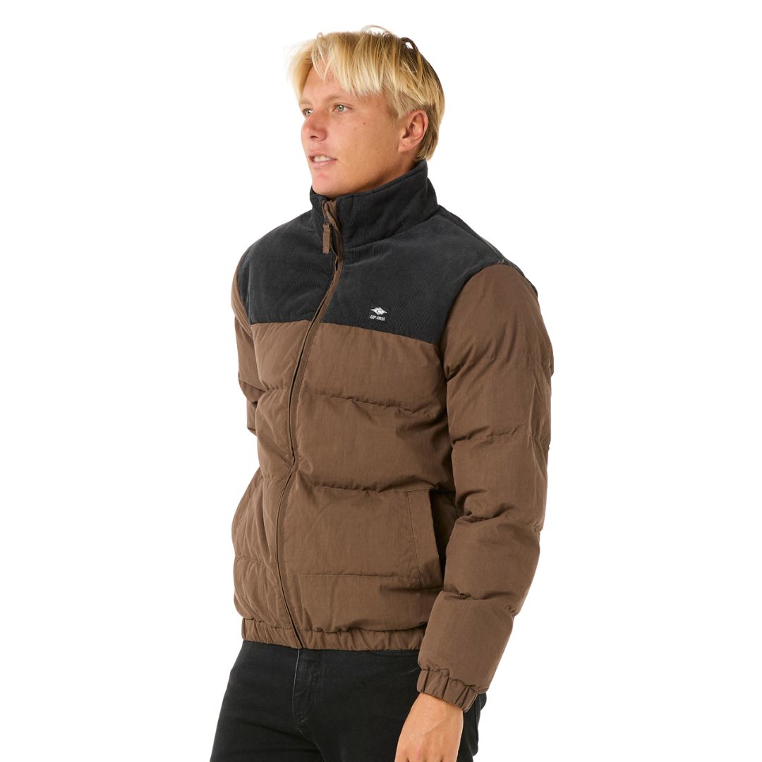 Vista lateral de la chaqueta Rip Curl Fade Out Cord Puffer marrón y negra, con modelo de perfil.