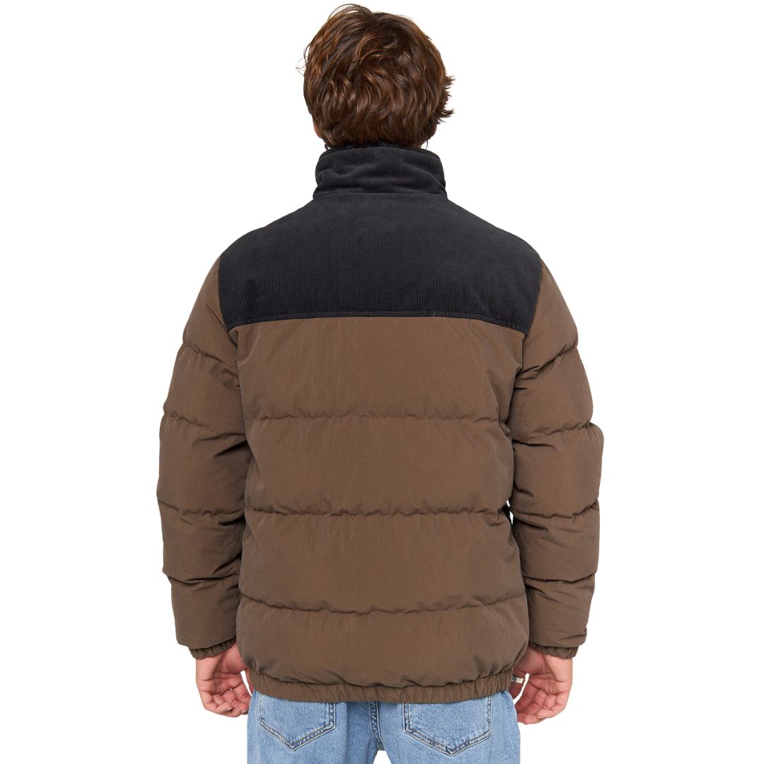 Modelo con chaqueta Rip Curl Fade Out Cord Puffer marrón/negra, vista frontal con manos en bolsillos.