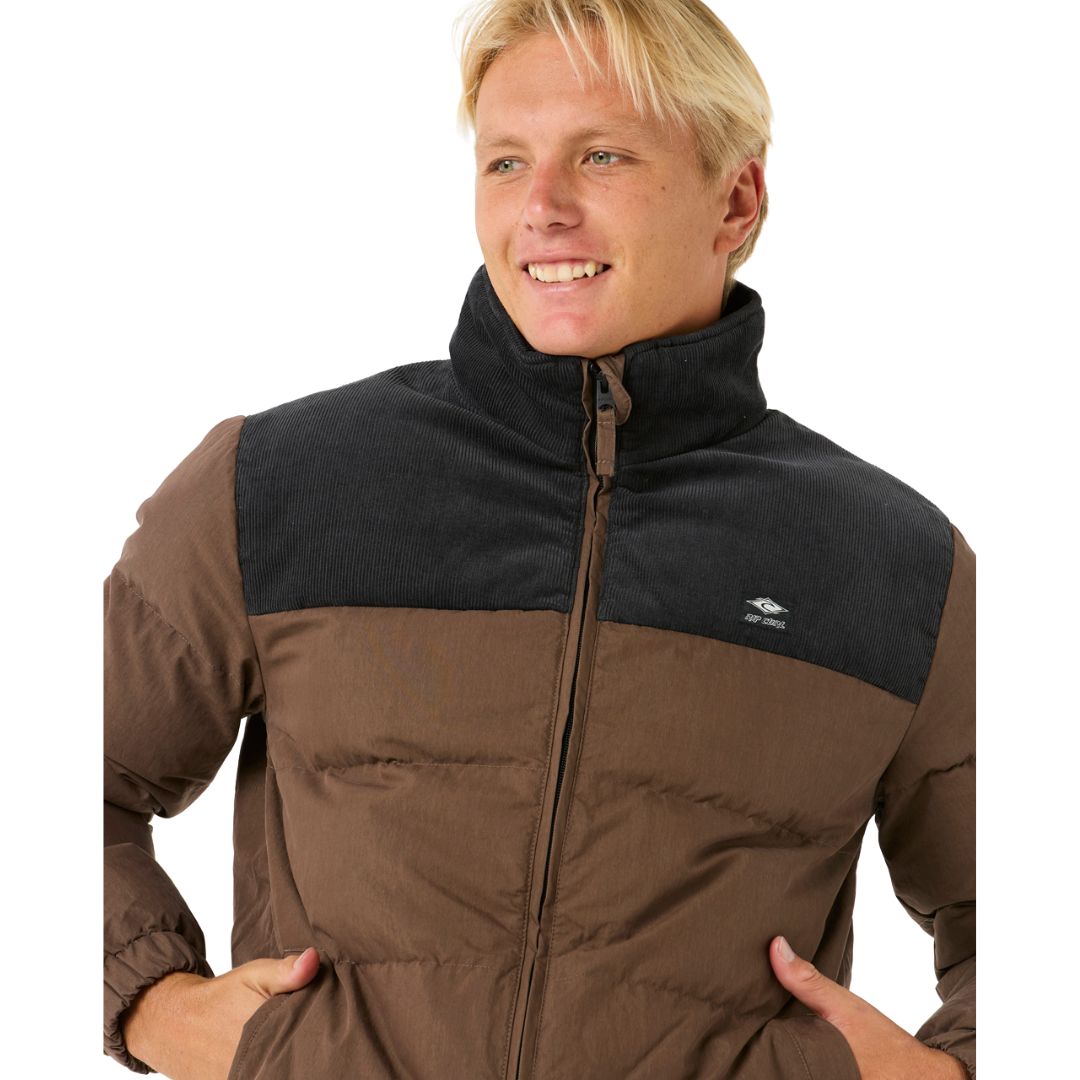 Chaqueta Rip Curl Fade Out Cord Puffer para hombre en marrón y negro, vista frontal con cremallera cerrada.