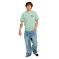Camiseta de surf RIP CURL HARDCORE TEE SERIES en Aloe, vista frontal de cuerpo completo mostrando el logotipo circular en el pecho y el corte oversize combinado con vaquero ancho.