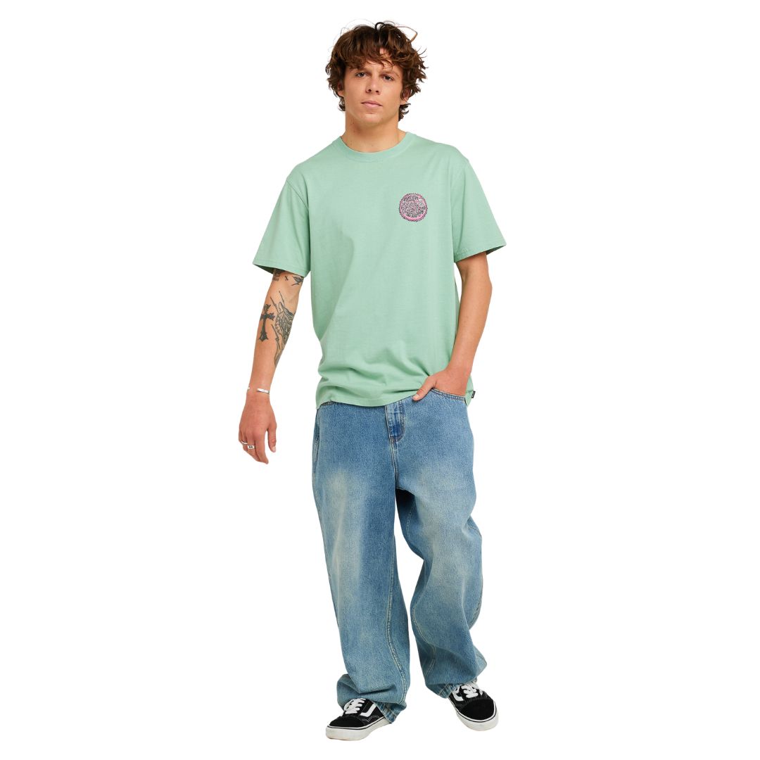 Camiseta de surf RIP CURL HARDCORE TEE SERIES en Aloe, vista frontal de cuerpo completo mostrando el logotipo circular en el pecho y el corte oversize combinado con vaquero ancho.