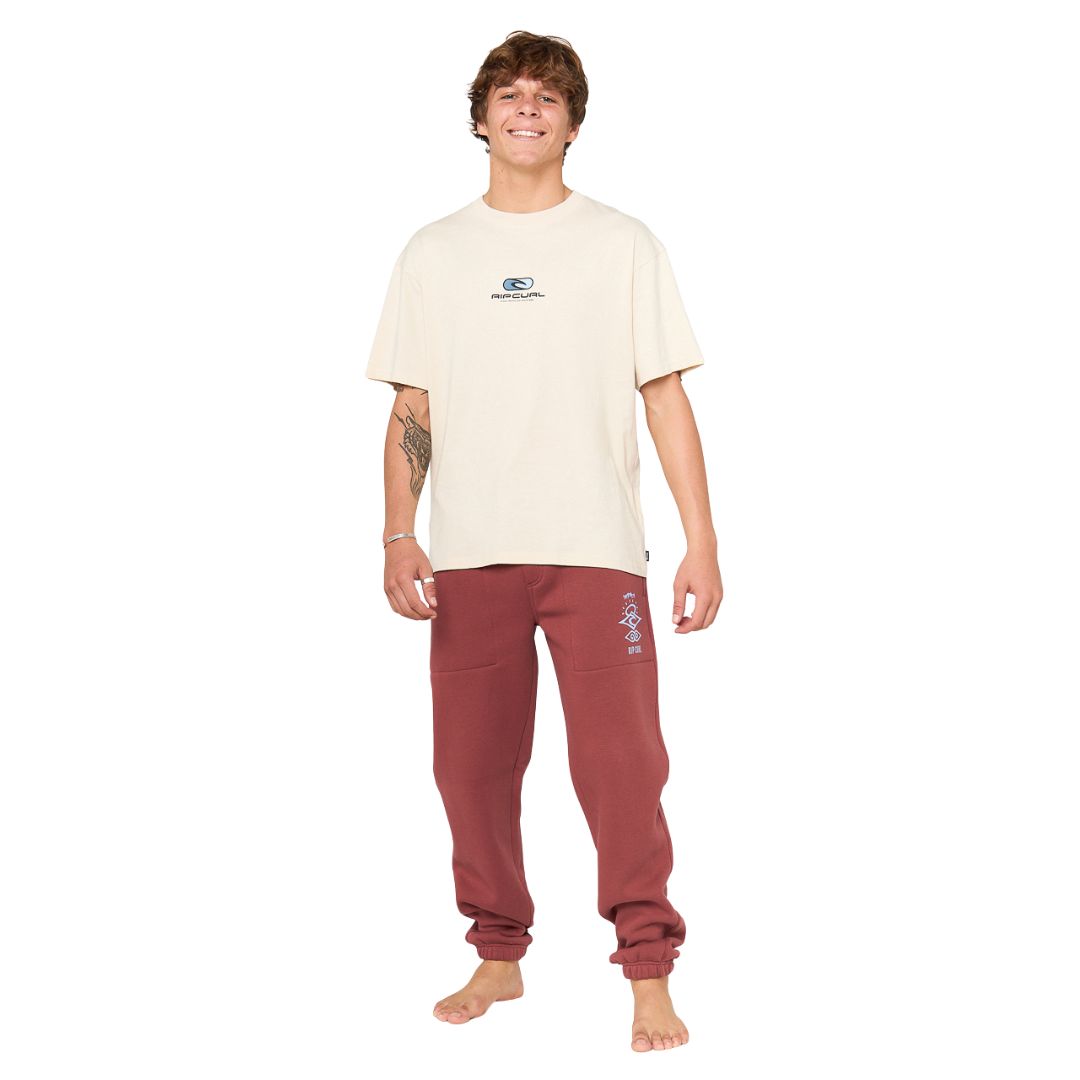 Modelo de pie vistiendo pantalón Rip Curl Icons of Surf en color Apple Butter y camiseta clara, estilo casual surf.