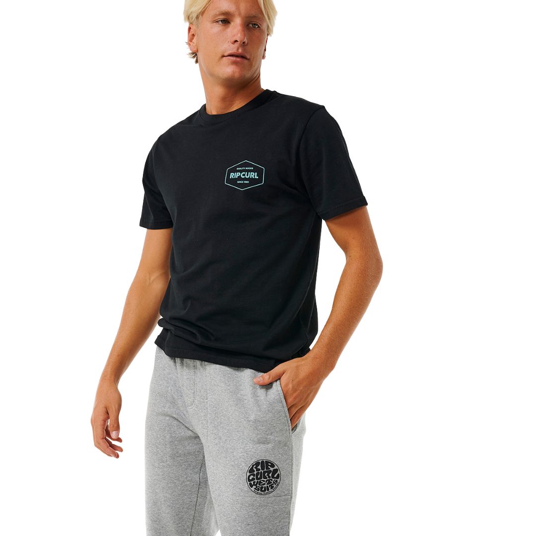 Modelo vistiendo pantalón Rip Curl Icons of Surf gris jaspeado y camiseta negra, en posición relajada de pie.