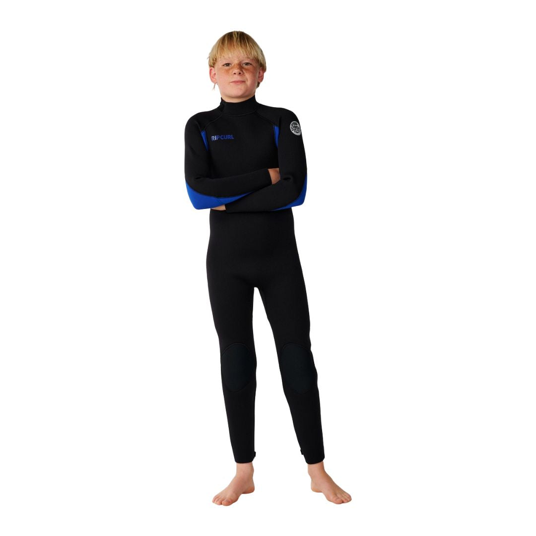Traje de neopreno infantil Rip Curl Trad Back Zip 4/3 en azul, vista frontal con brazos cruzados, detalle del logo RIPCURL y el parche de hombro en color azul.