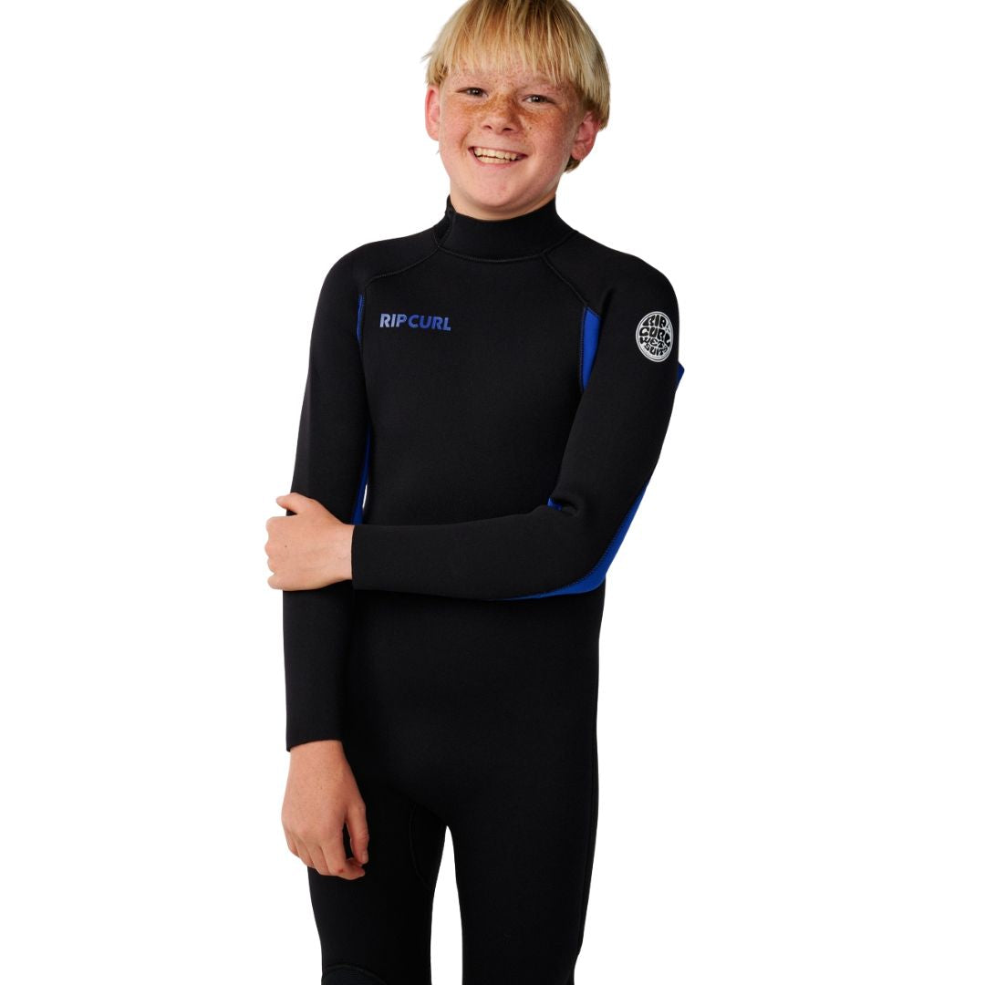 Traje de neopreno Rip Curl Kids Trad Back Zip 4/3 en azul, retrato frontal con brazos cruzados mostrando el cuello alto y el acabado del cuello del traje infantil.